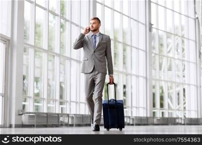 business trip, corporate and people concept - young businessman walking with travel bag along office building or airportand calling on smartphone. businessman with travel bag calling on smartphone