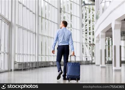 business trip, corporate and people concept - young businessman walking with travel bag along office building or airport. businessman with travel bag walking along office