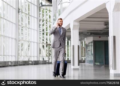 business trip, corporate and people concept - young businessman walking with travel bag along office building or airport and calling on smartphone. businessman with travel bag calling on smartphone