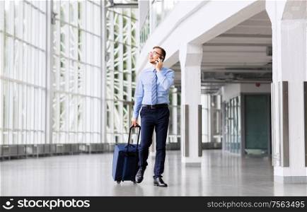 business trip, corporate and people concept - young businessman walking with travel bag along office building or airport and calling on smartphone. businessman with travel bag calling on smartphone