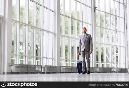 business trip, corporate and people concept - young businessman walking with travel bag along office building or airport. businessman with travel bag walking along office