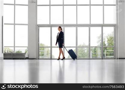 business trip, corporate and people concept - young businesswoman walking with travel bag along office building or airport. businesswoman with travel bag walking along office