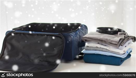 business trip, luggage and clothing concept - close up of travel bag, shirts, trousers and belt over snow effect over snow effect