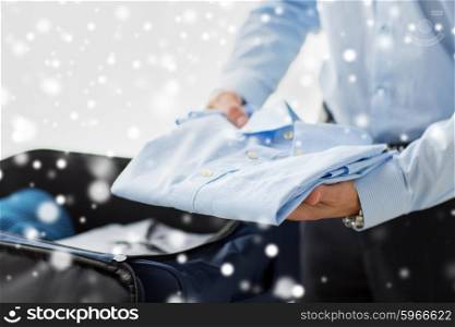 business, trip, luggage and people concept - close up of businessman packing clothes into travel bag over snow effect