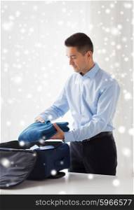 business, trip, luggage and people concept - happy businessman packing clothes into travel bag over snow effect over snow effect