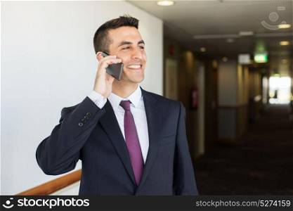 business trip, people and communication concept - happy smiling businessman calling on smartphone at hotel corridor. smiling businessman calling on smartphone at hotel