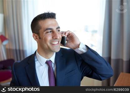 business trip, people and communication concept - happy smiling businessman calling on smartphone at hotel room. businessman calling on smartphone at hotel room