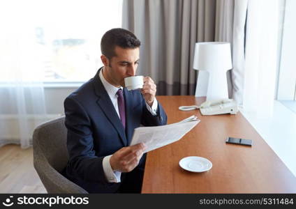 business trip, people and mass media concept - businessman reading newspaper and drinking coffee at hotel room. businessman reading newspaper and drinking coffee