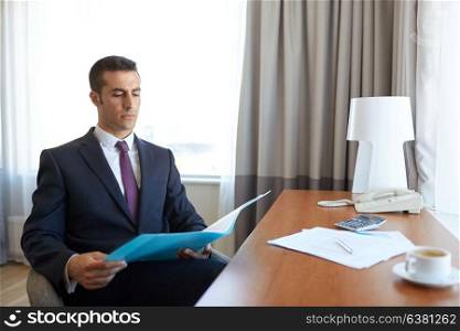business trip, people and paperwork concept - businessman with papers in folder working at hotel room. businessman with papers working at hotel room