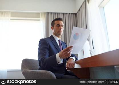 business trip, people and paperwork concept - businessman with papers working at hotel room. businessman with papers working at hotel room