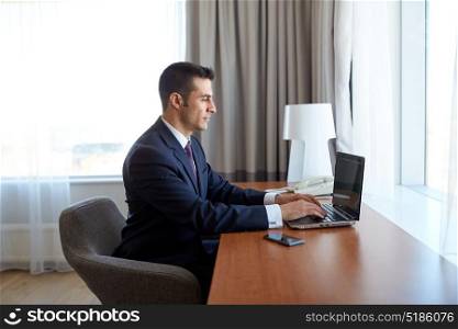 business trip, people and technology concept - businessman typing on laptop at hotel room. businessman typing on laptop at hotel room