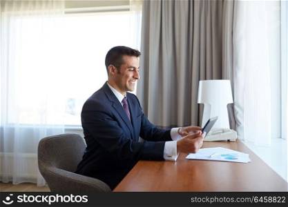 business trip, people and technology concept - businessman with tablet pc computer and papers working at hotel room. businessman with tablet pc working at hotel room