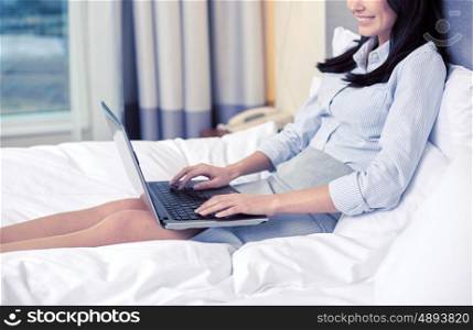 business trip, people and technology concept - smiling businesswoman with laptop computer typing in bed at hotel
