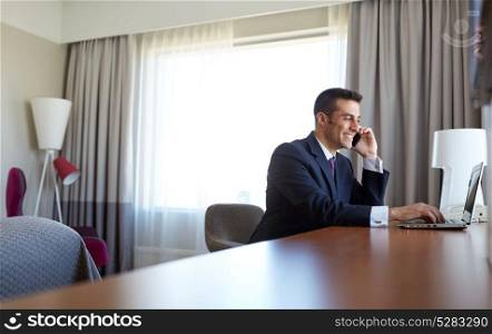business trip, people, communication and technology concept - businessman with laptop computer calling on smartphone at hotel room. businessman with laptop and smartphone at hotel