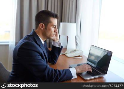 business trip, people, communication and technology concept - businessman working with laptop computer calling on smartphone at hotel room. businessman with laptop and smartphone at hotel