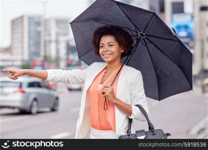business trip, transportation and people concept - young smiling african american woman with umbrella catching taxi at city street