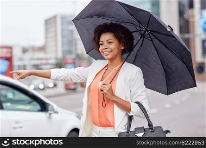 business trip, transportation and people concept - young smiling african american woman with umbrella catching taxi at city street