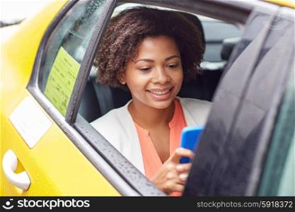 business trip, transportation, travel, gesture and people concept - young smiling african american woman texing on smartphone in taxi at city street