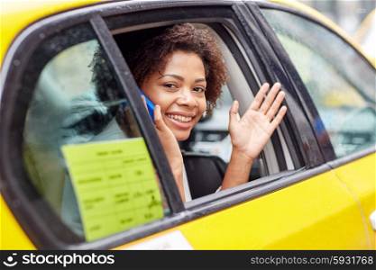 business trip, transportation, travel, gesture and people concept - young smiling african american woman calling on smartphone and waving hand from taxi at city street