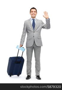 business trip, traveling, luggage and people concept - happy businessman in suit with travel bag and air ticket waving hand