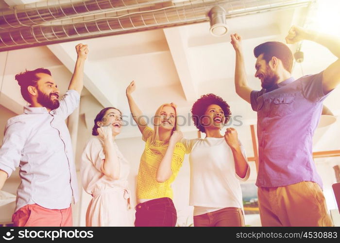 business, triumph, gesture, people and teamwork concept - happy creative team raising hands up and celebrating victory in office