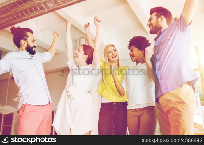 business, triumph, gesture, people and teamwork concept - happy creative team raising hands up and celebrating victory in office