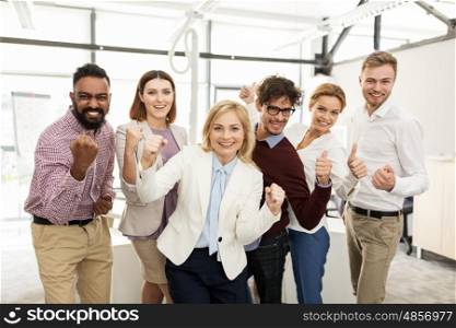 business, triumph, gesture, people and teamwork concept - happy creative team showing fists and celebrating victory at office
