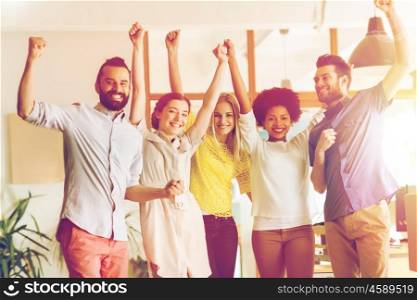 business, triumph, gesture, people and teamwork concept - happy international creative team raising hands up and celebrating victory in office