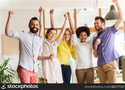 business, triumph, gesture, people and teamwork concept - happy international creative team raising hands up and celebrating victory in office