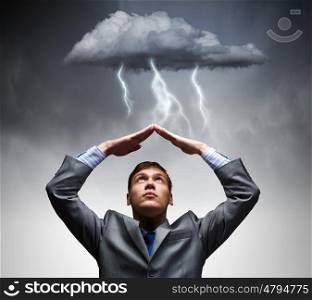 Business troubles. Businessman sitting under rain protecting head with arms