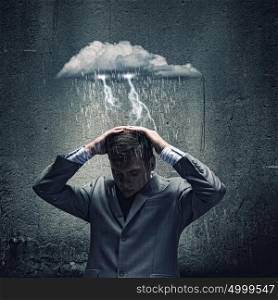 Business troubles. Businessman sitting under rain protecting head with arms