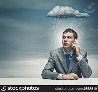 Business troubles. Businessman sitting under rain talking on mobile phone