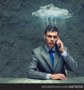 Business troubles. Businessman sitting under rain talking on mobile phone
