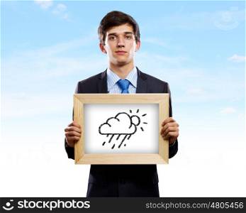 Business troubles. Young businessman holding frame with weather drawings