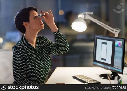 business, vision and overwork concept - female graphic designer with dry eye syndrome using drops at night office. female designer using eye drops at night office