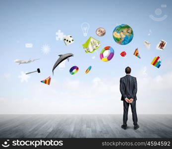 Business vision. Back view of confident businessman looking at city with items flying in air. Elements of this image are furnished by NASA