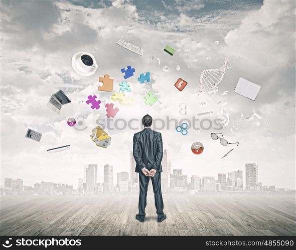 Business vision. Back view of confident businessman looking at city with items flying in air