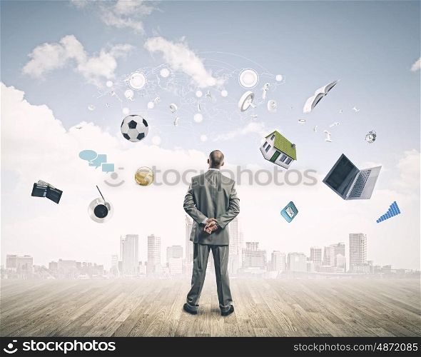 Business vision. Back view of confident businessman looking at city with items flying in air