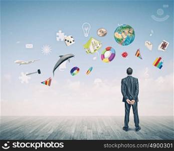 Business vision. Back view of confident businessman looking at city with items flying in air. Elements of this image are furnished by NASA