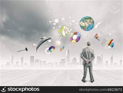 Business vision. Back view of confident businessman looking at city with items flying in air. Elements of this image are furnished by NASA