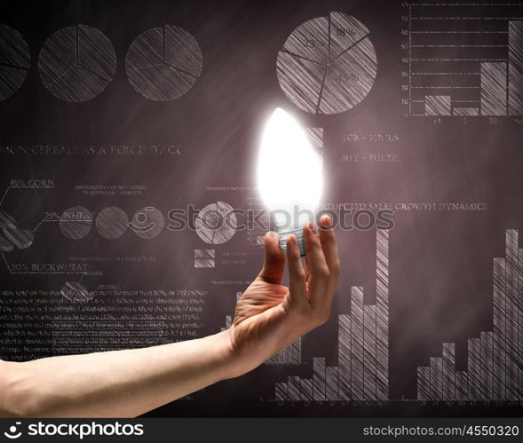 Business vision. Close up of hand holding light bulb with sketches at background