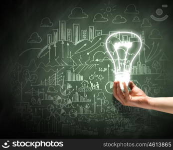 Business vision. Close up of hand holding light bulb with sketches at background