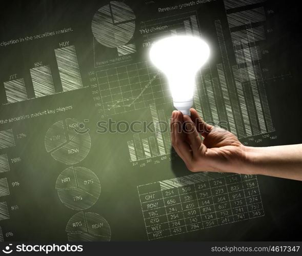 Business vision. Close up of hand holding light bulb with sketches at background