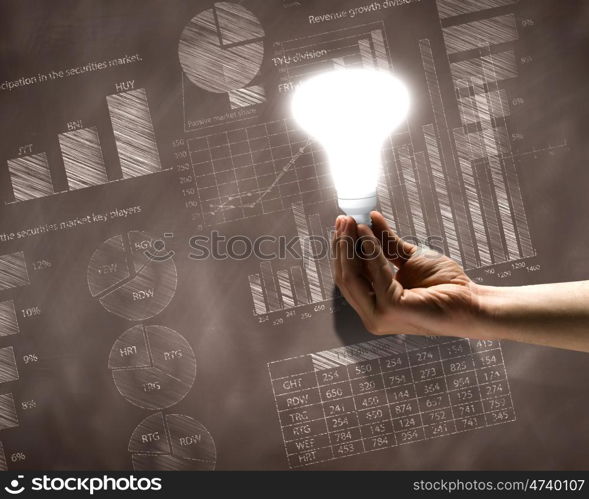 Business vision. Close up of hand holding light bulb with sketches at background