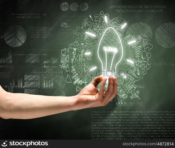 Business vision. Close up of hand holding light bulb with sketches at background