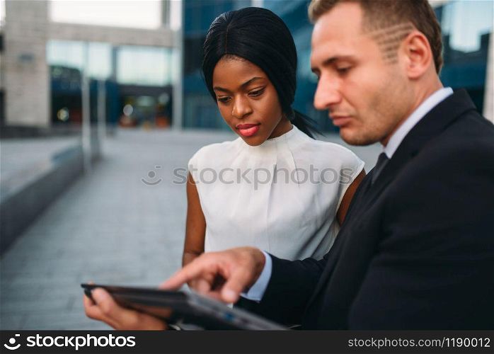 Business woman and businessman looks on laptop screen, outdoors meeting of partners, modern office building on background, partnership negotiations during the lunch break. Business woman and businessman looks on laptop