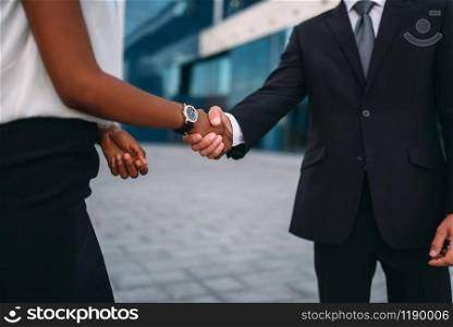 Business woman and businessman shake hands, outdoors meeting of partners, modern office building on background, partnership negotiations. Successful businesspeople. Business woman and businessman shake hands