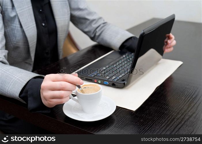 business woman at table with netbook, stirs coffee in cup, cropped down shoulders