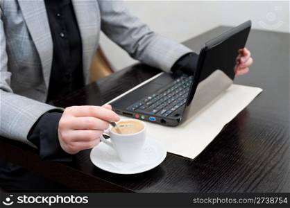business woman at table with netbook, stirs coffee in cup, cropped down shoulders