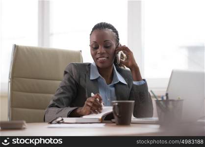 Business woman calling phone and writing something in her schedule book and papers at office workplace